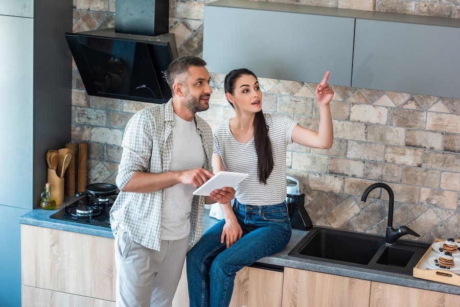 Man and woman in kitchen customizing smart home features using a tablet.