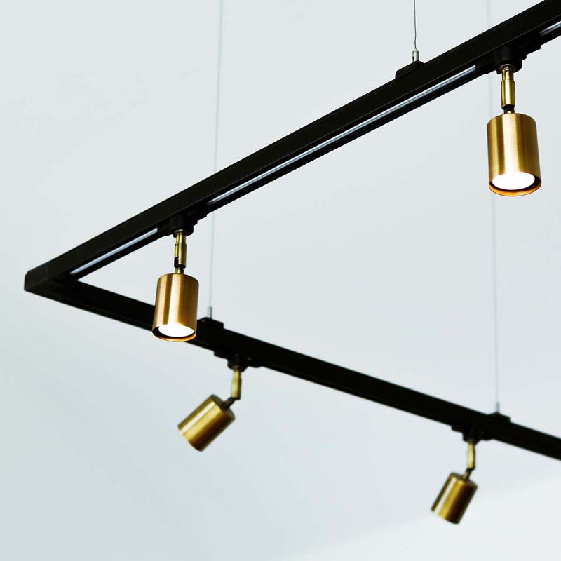 Black rectangular track fixture suspended from the ceiling, featuring multiple pivoting cylinder lights.