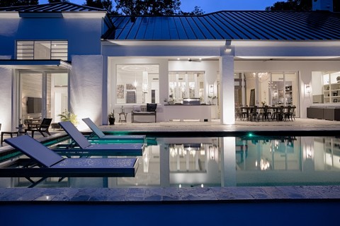 A Sophisticated ultra-modern home seen from across an inground pool with stunning interior lighting through expansive windows.
