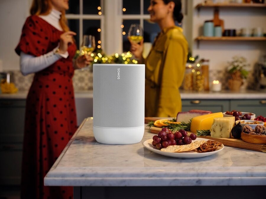A Sonos speaker on a kitchen island amidst a holiday get-together with two women chatting in the background.