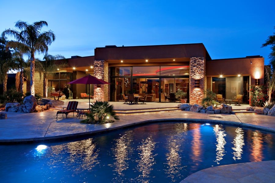 The backyard of a well-lit home with a pool and palm trees.