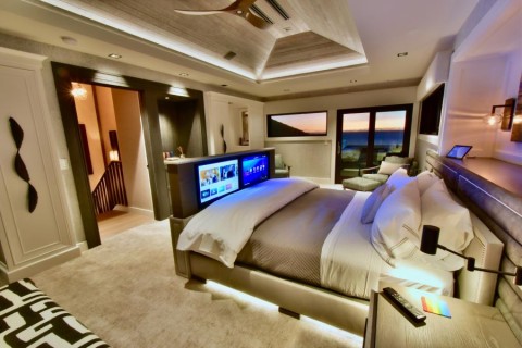 A bedroom with in-ceiling speakers, a TV that rises from the foot of the bed, and a Control4 touchscreen.
