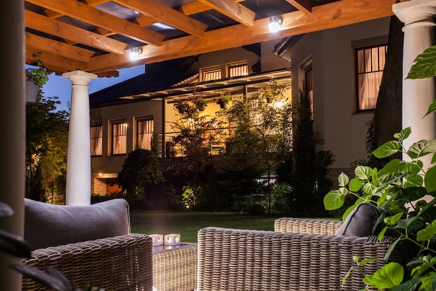 A pergola in a backyard at night with ceiling lights.