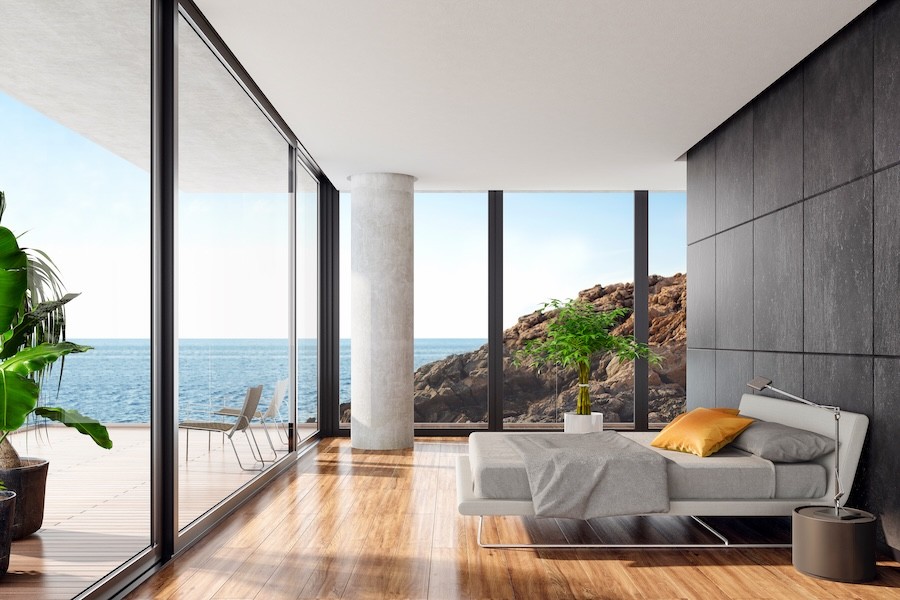 Sonance speakers are hidden in the ceiling of a modern bedroom overlooking the ocean.